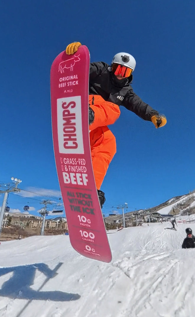 Person snowboarding with a pink Chomps snowboard in a snowy landscape.