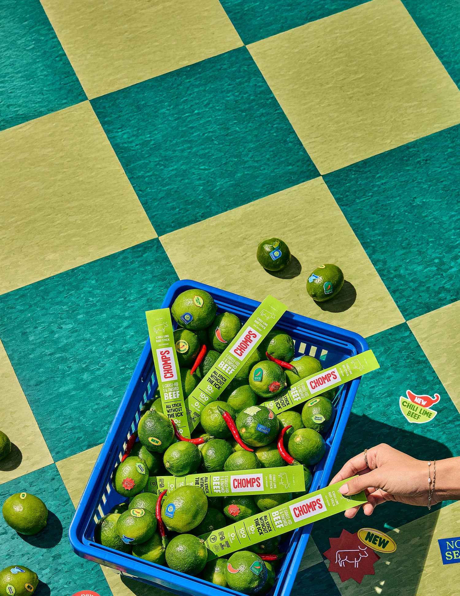 Basket of green limes with Chomp's Meat Sticks on a checkered green and blue floor.