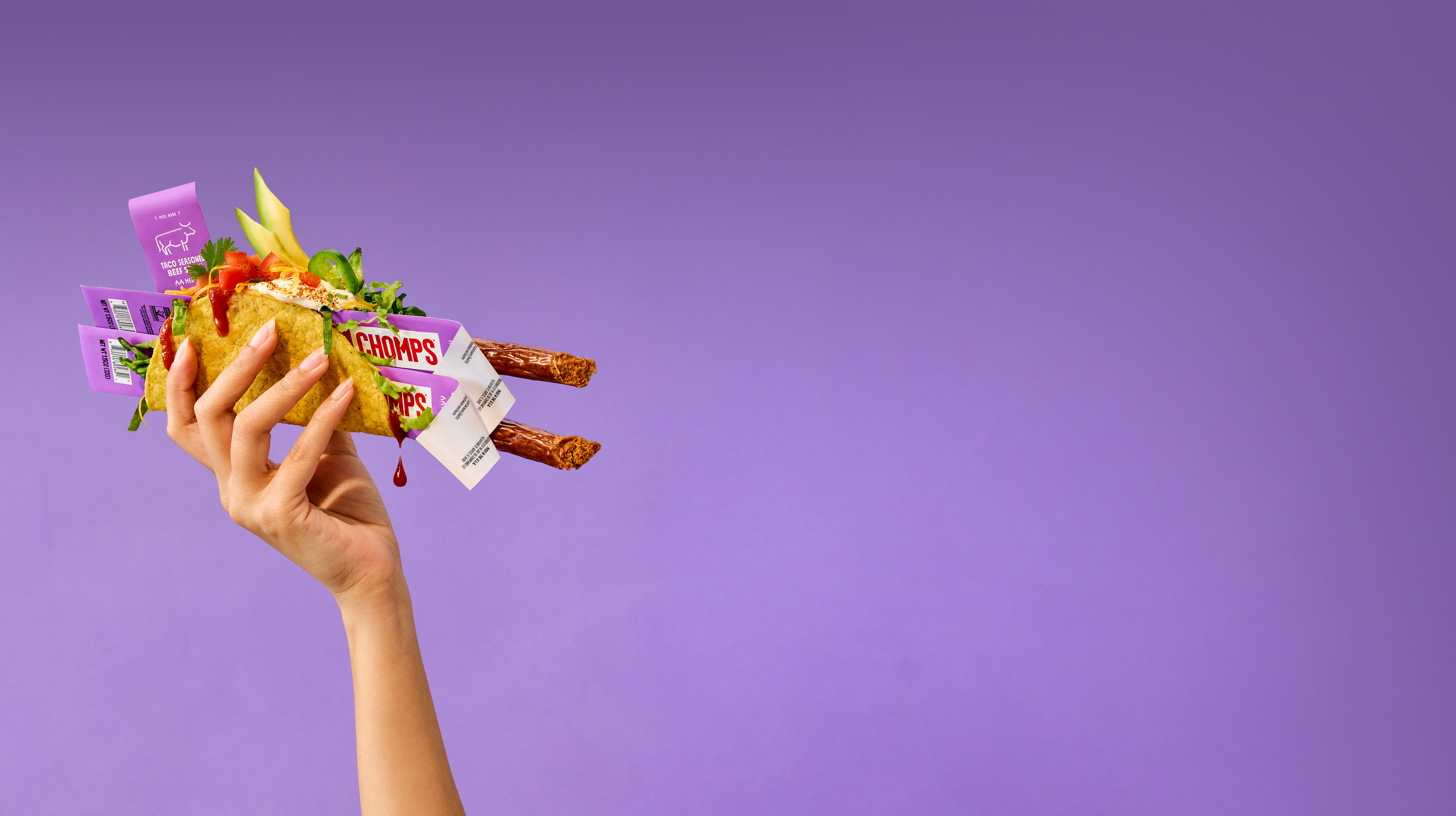 Hand holding a variety of snack packages against a purple background