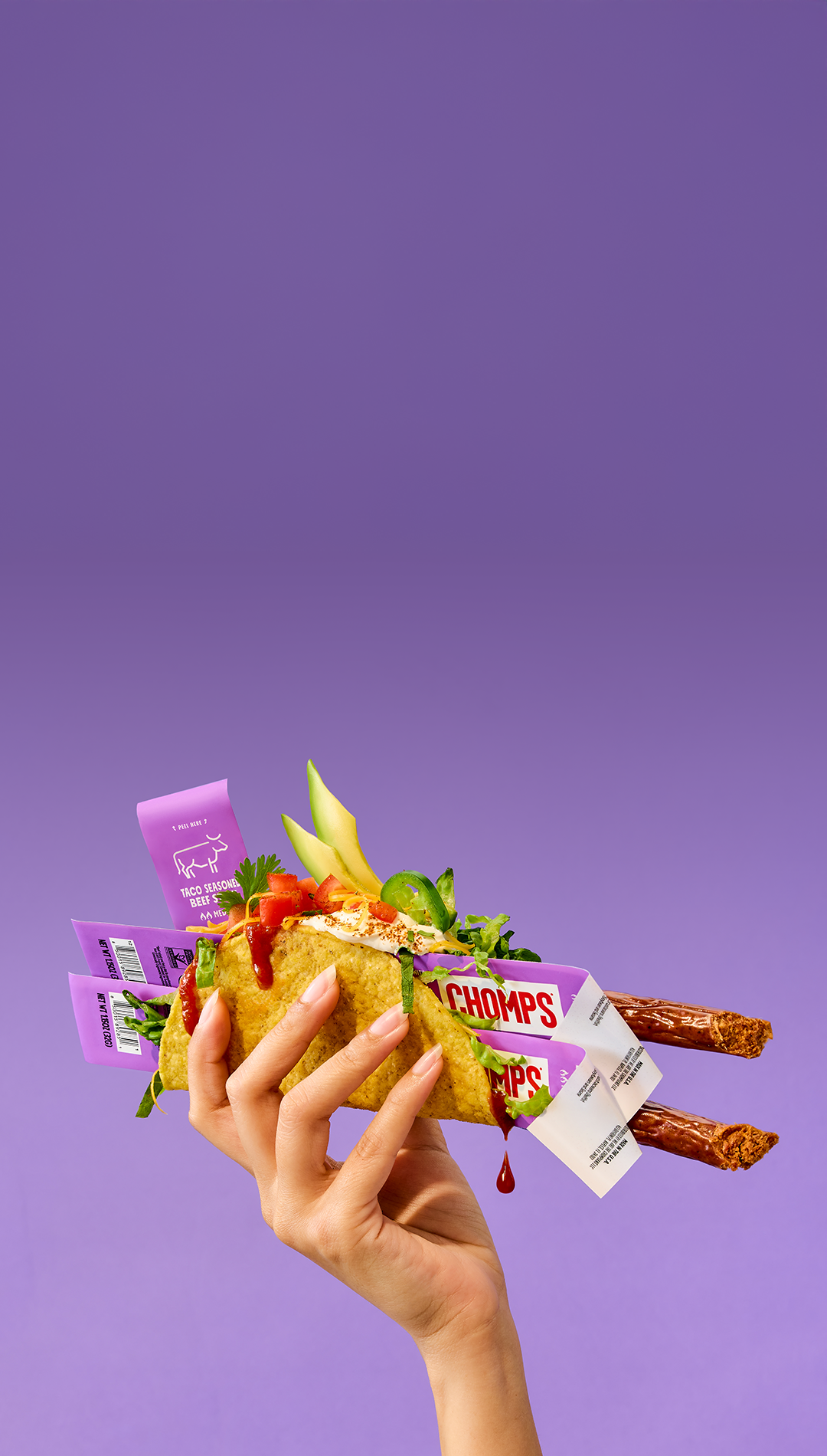 Hand holding a taco with Chomps snack packaging on a purple background