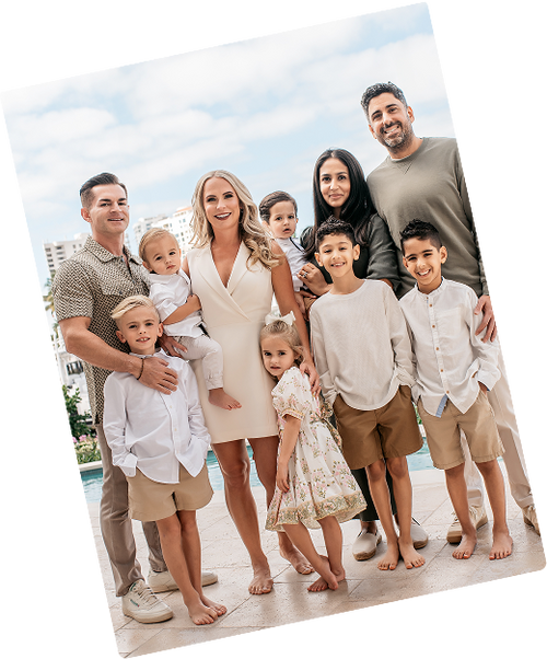 A family portrait showing Pete and Rashid's family, standing together outdoors on a tiled patio with a pool and sky in the background. 