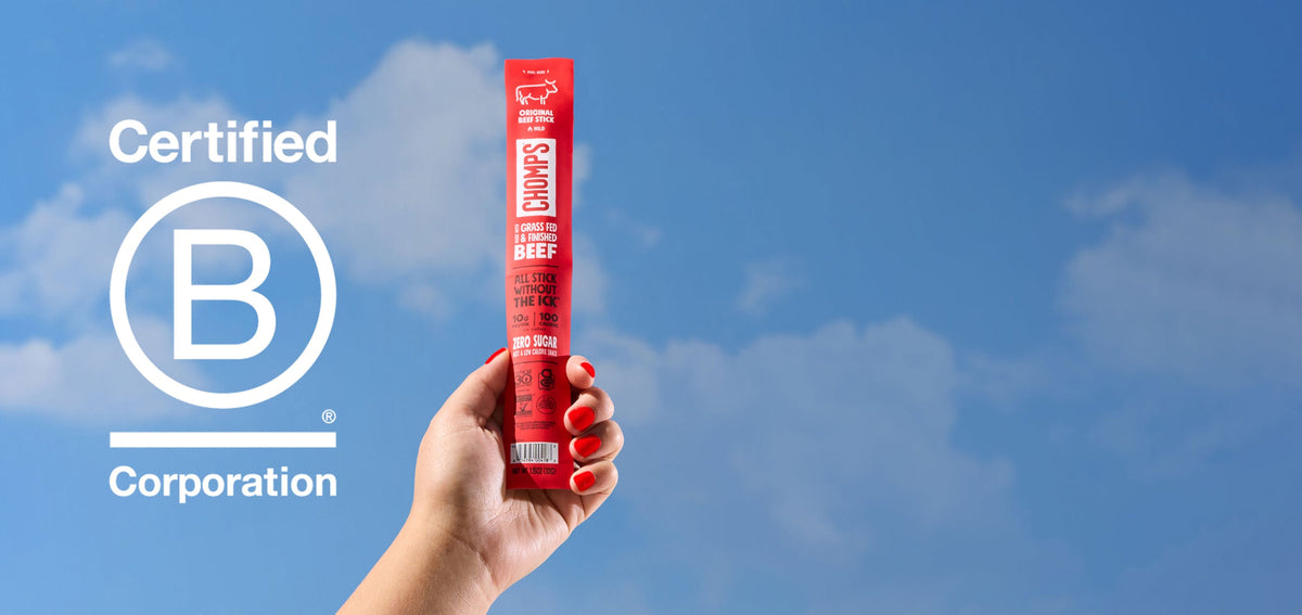 A hand with red nail polish holds a Chomps Original Beef Stick against a blue sky with clouds. A large Certified B Corporation logo is displayed on the left