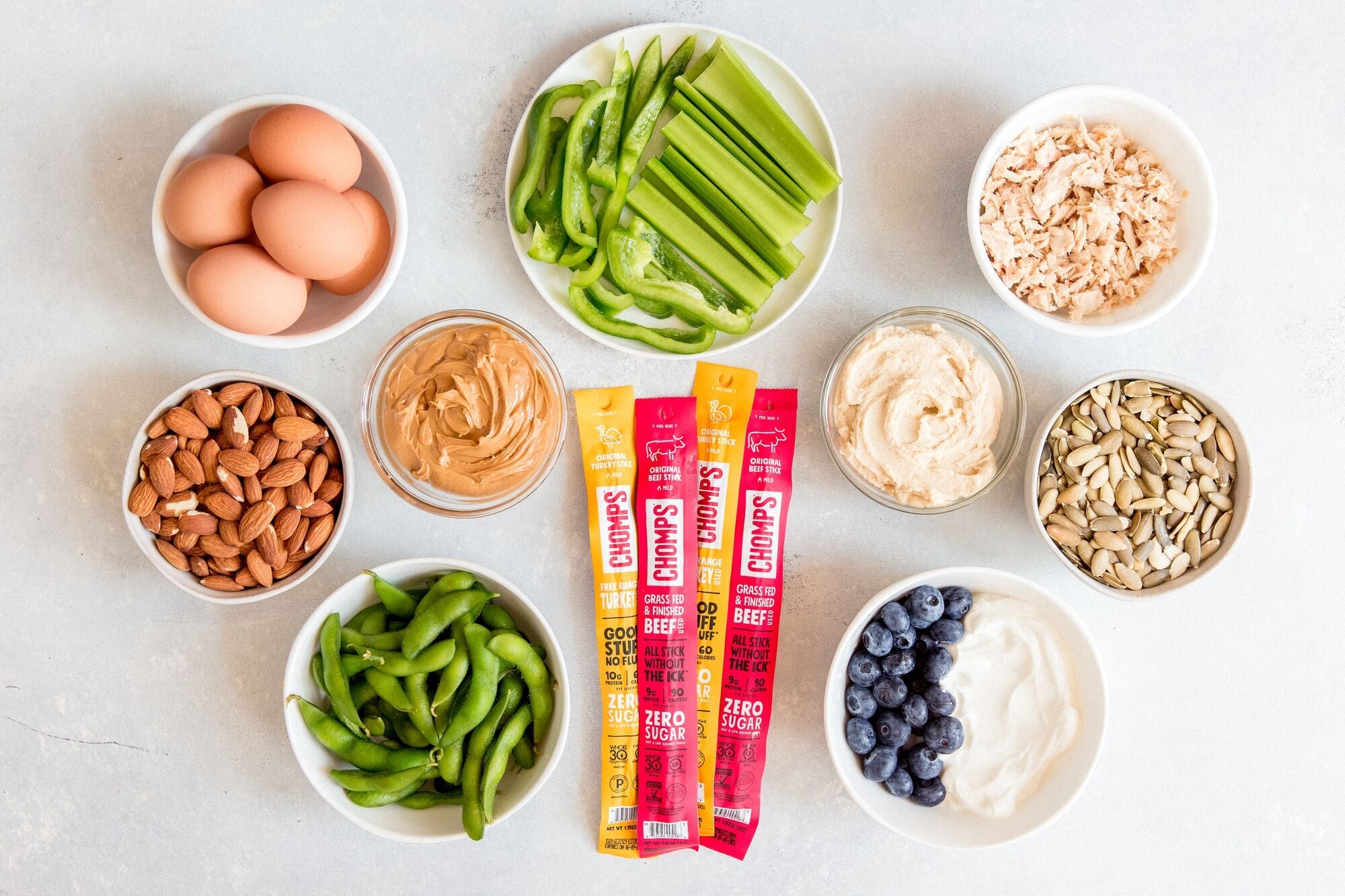 An assortment of Chomps sitting amongst bowls of healthy snack options