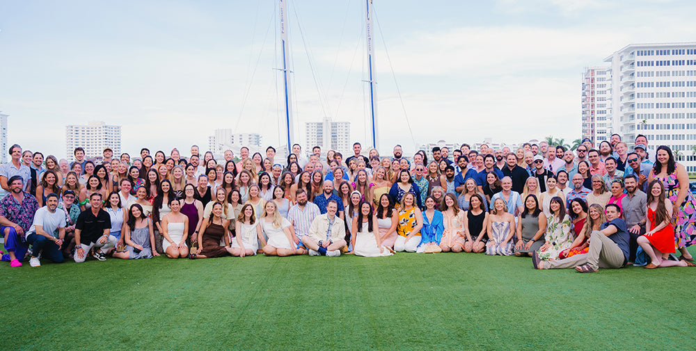 Chomps employees posing together on green artificial turf outdoors, with buildings and tall masts visible in the background under a pale sky.